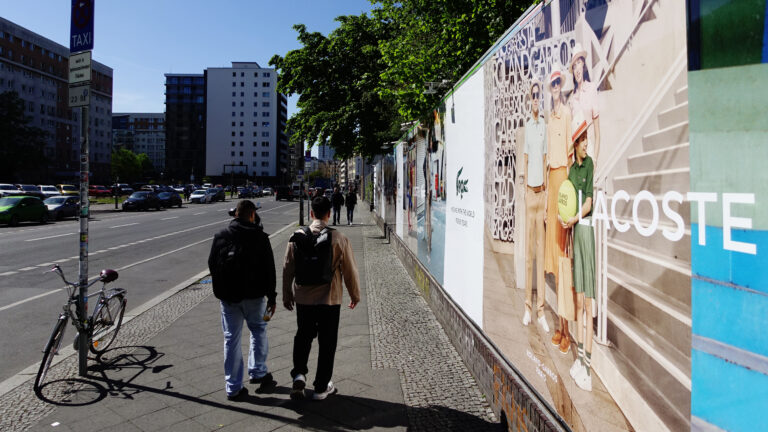 Lacoste Werbung an einer belebten Straße mit Fußgängern.